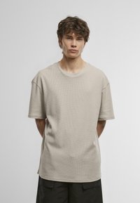 Tricou bej cu mânecă scurtă, fabricat dintr-un material texturat, cu un guler rotund și croială lejeră, asortat cu pantaloni scurți închiși la culoare.