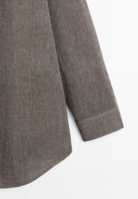 Bruine gestructureerde lange mouw met boorden en een gebogen zoom op een witte achtergrond, met details van de stofstructuur.