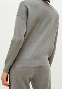 Szary dziergany sweter o luźnym kroju, z długimi rękawami i prążkowanym dołem. Miękka tekstura i prosty design bez widocznych wzorów.