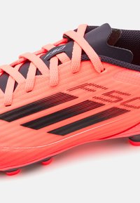Botas de fútbol en coral brillante con rayas negras, parte superior sintética texturizada y lengua negra. Cuenta con cordones a juego y tacos moldeados.