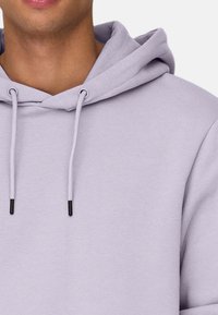 Helle Lavendel-Haube aus Baumwollmischung, mit einer Kordelzugkapuze mit schwarzen Spitzen und einer weichen, glatten Textur.