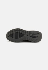 Black rubber shoe sole featuring a textured pattern with grooves, ridges, and branding details. Flat and rounded shape for stability.