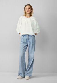 Witte gestructureerde blouse met losse, ballonmouwen, gecombineerd met hoge taille lichtblauwe wijde jeans en witte platform sneakers.