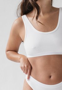 Weißer Baumwoll-Bralette mit Rundhalsausschnitt und breiten Trägern, kombiniert mit passender weißer Unterwäsche. Glatte Textur, enganliegendes Design.