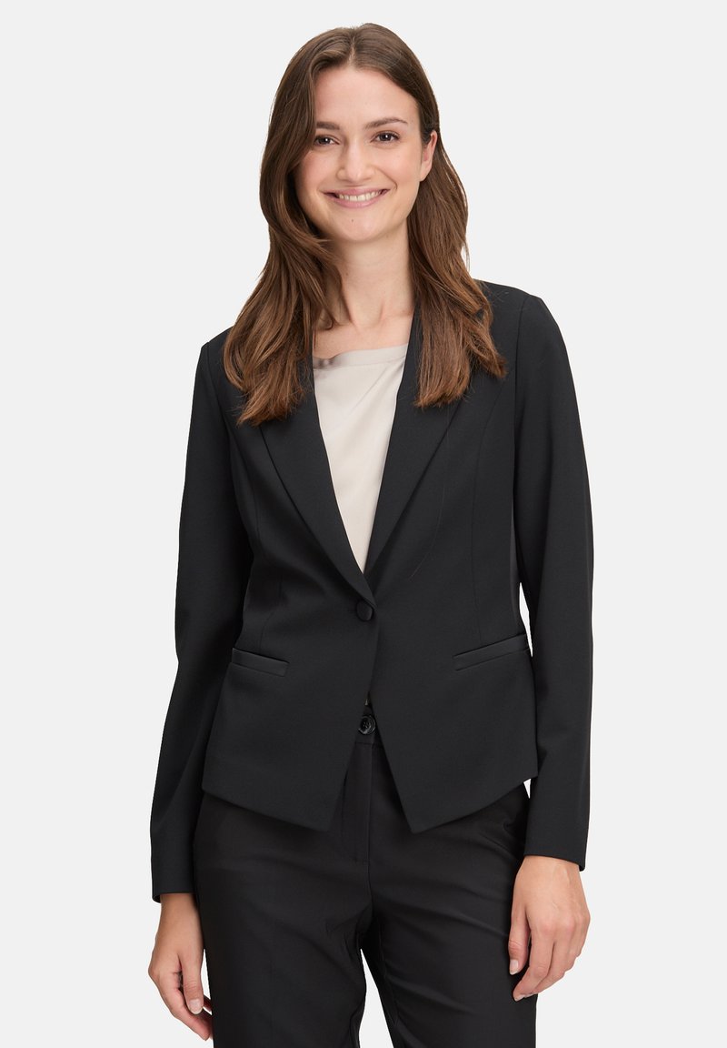 Schwarzer maßgeschneiderter Blazer mit einem einzelnen Knopfverschluss, zwei Vordertaschen und einer glatten Textur, kombiniert mit einem hellen Oberteil.