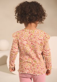 Roosa pikkade varrukatega topp, millel on sooniline tekstuur, oranži ja rohelise lillemustriga ning volangidega õlad. Lühendatud disain.