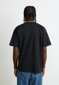 T-shirt en coton noir à manches courtes et col rond ; il présente un ourlet droit et une coupe décontractée, associé à un jean en denim bleu clair.