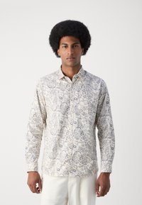 Camisa de manga larga abotonada en crema con intrincado patrón de paisley azul, con cuello clásico y tapeta de botones, textura de tela de algodón.