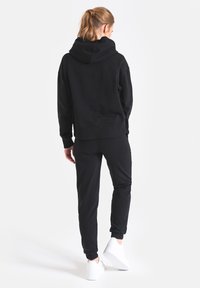 Czarna bluza z kapturem i dopasowane spodnie dresowe wykonane z miękkiego materiału, z dużym kapturem i elastycznymi ściągaczami; w zestawie z białymi trampkami.