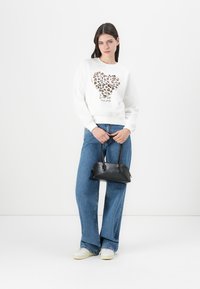 Weißes Sweatshirt mit einem Herzdesign im Leopardenmuster, kombiniert mit hellblauen Schlagjeans und einer kleinen schwarzen Handtasche.
