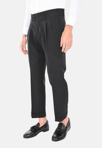 Pantaloni neri plissettati con taglio dritto, dotati di due chiusure a bottone in vita e risvolti, abbinati a mocassini neri.