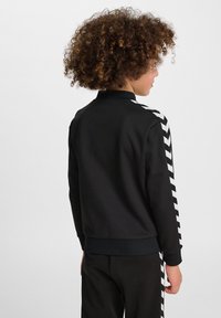 Felpa nera con colletto alto e strisce a V bianche sulle maniche; texture morbida, polsini aderenti e design pulito sul retro.