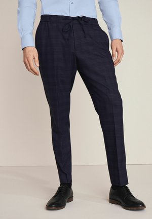 Pantalons à carreaux navy avec une taille élastique et un cordon de serrage, coupe fuselée et texture lisse. Associés à des chaussures noires en cuir.