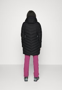Juodas pūkinis švarkas su gobtuvu, pasižymintis chevrono quilted dizainu. Dėvimas ant rožinių kelnių ir pilkų batų su akcentais.