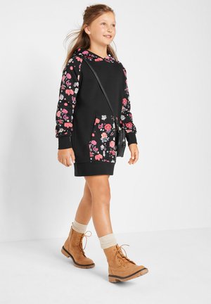 Schwarzes Blumen-Hoodie-Kleid mit langen Ärmeln und Fronttasche. Getragen mit tanfarbenen Schnürstiefeln, cremefarbenen, umgeschlagenen Socken und einer kleinen schwarzen Tasche.