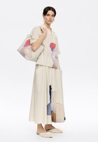 Beige overhemd en lange rok met kleurrijke kunstprints, textuur rijke crèmekleurige totebag en fluffy slider schoenen. Glad stof en casual stijl.