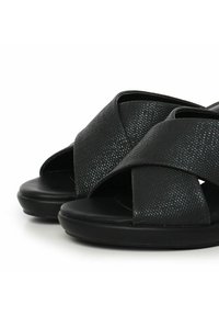 Sandalias negras con una superficie texturizada, que cuentan con un diseño de tiras cruzadas y una suela lisa. Forma redondeada para mayor comodidad y facilidad de uso.
