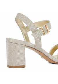 Glittery silver block-heeled sandal with adjustable ankle strap, textured upper, and gold-tone buckle accent. Open toe design.