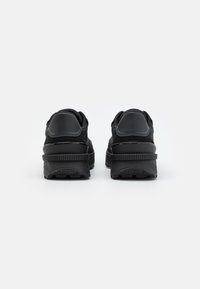 Zapatillas negras con parte superior texturizada, cuello acolchado y suela de goma. Presenta un diseño aerodinámico y sutiles acentos azules cerca del talón.