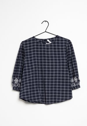 Marineblå ternet bluse med trekvartlange ærmer, der har hvidt rutemønster og broderede detaljer ved manchetterne. Letvægtsstof.