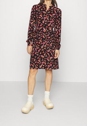 Een zwarte jurk met een bloemenpatroon in roze en rood, lange mouwen en een knoopsluiting, gecombineerd met crèmekleurige klompen en witte sokken.