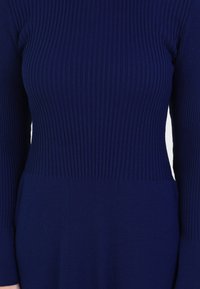 Abito a maglia blue navy a coste con maniche lunghe, caratterizzato da una parte superiore testurizzata e una sezione inferiore liscia, che evidenzia una silhouette aderente.