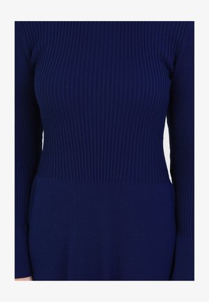Tmavě modré žebrované pletené šaty s dlouhými rukávy, které mají strukturovanou horní část a hladkou dolní část, zdůrazňující přiléhavý siluetu.