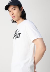 Hvid bomulds t-shirt med korte ærmer, der har et sort "Just Do It" grafik. Sammen med en sort kasket, der viser et enkelt design.