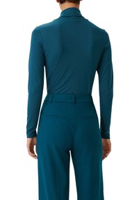 Türkiser Langarmoberteil mit hohem Kragen, taillierter Passform, weichem Material, kombiniert mit passenden maßgeschneiderten Hosen mit Gesäßtaschen.