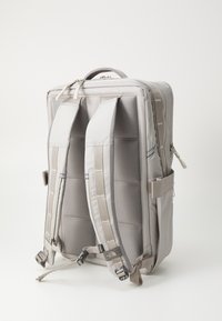 Pelēks mugursoma ar mīkstinātām plecu siksnām, rāvējslēdzēja aizdari un sānu kabatām. Tekstūra ir gluda, ar strukturētu taisnstūra formu.