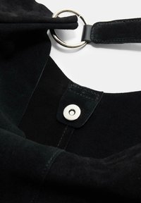 Sac à main en daim noir avec une texture lisse, arborant un anneau en métal argenté et un détail de fermeture à pression. Le design comprend des bords arrondis.
