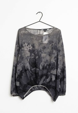 Blouse à manches longues pour femme avec motif floral noir et gris, col rond et ourlet incurvé, suspendue à un cintre noir.