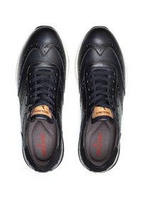 Zapatillas de cuero negro con un acabado texturizado, que presentan un diseño con cordones, suela blanca en contraste y un logo en relieve en la lengüeta.