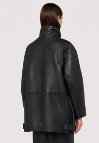 Svart läderjacka med hög krage, med en boxig design, synliga sömmar och tryckknappar i fållen för justerbar passform.