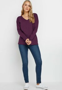 Lila långärmad v-ringad topp i kombination med åtsittande mörkblå jeans och vita sneakers, med en avslappnad passform och mjuk textur.