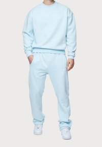 Conjunto de sudadera y pantalones deportivos en azul claro, hecho de tejido suave. Presenta puños y cintura acanalados con un pequeño detalle de logo en el pecho y el muslo.