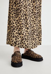 Zoccoli con stampa leopardata e texture pelosa, con suole nere a piattaforma, abbinati a una gonna con stampa leopardata coordinata.