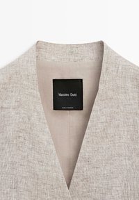 Lichtbeige linnen colbertkraag met een zwart label waarop "Massimo Dutti" staat en "Made in Morocco" aan de binnenkant van de hals.