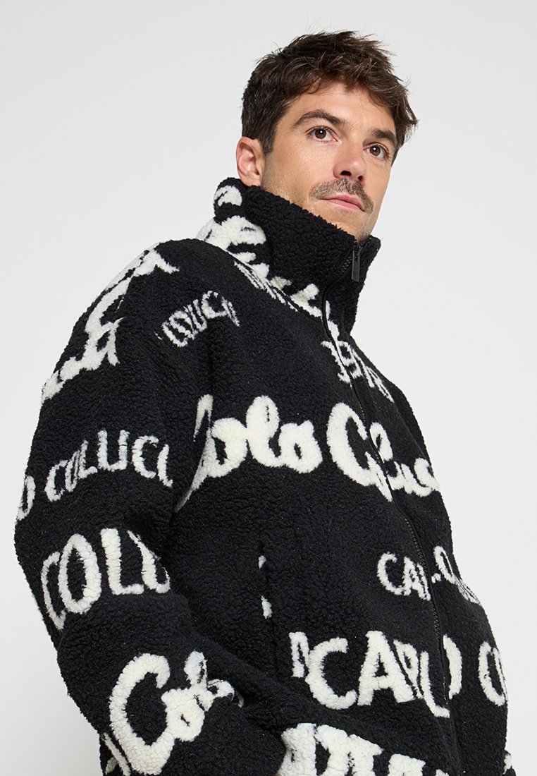 Schwarz-weiße Fleecejacke mit hohem Kragen, Reißverschluss und einem wiederholten Logomuster in kontrastierenden Farben. Weicher Stoff und lässige Passform.