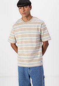 Beige striped t-shirt made of cotton. Features thin white and olive green stripes. Crew neck design with short sleeves and a logo detail at the hem.