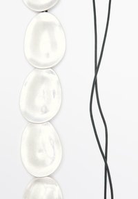 Collana con pendente ovale in argento, dal texture liscia, infilata su una corda nera. Presenta cinque elementi lucidi e riflettenti.