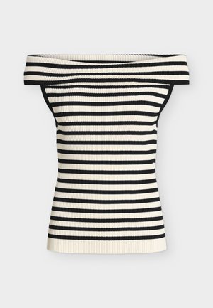 Femme portant un haut rayé noir et blanc à épaules dénudées, un short noir taille haute, des sandales noires, tenant un grand sac fourre-tout marron, debout sur un fond blanc.