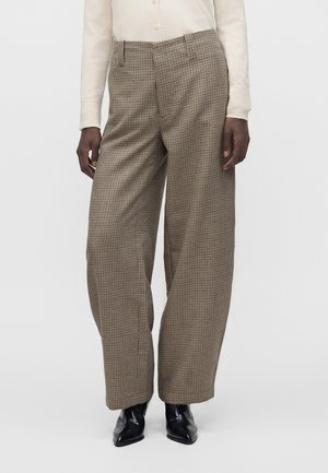 Person wearing high-waist wide-leg brown checkered trousers, cream long-sleeve shirt, and black pointed-toe ankle boots.