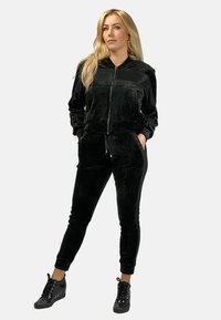 Czarny welurowy dres składający się z kurtki na zamek z bocznymi kieszeniami i dopasowanych spodni, oba z gładką fakturą i elastycznymi mankietami.