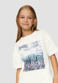 Weißes T-Shirt aus Baumwolle mit einer quadratischen Grafik einer Stadtlandschaft und dem Text "DREAMING NEW YORK" in Pink. Es hat einen lockeren Schnitt und kurze Ärmel.