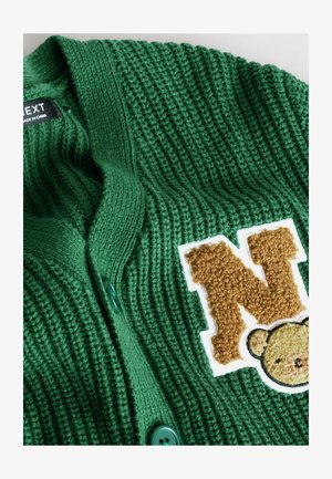 Zeleni pleteni kardigan z teksturirano površino, dvema zelenima gumboma in puhasto rjavo črko "N" z aplikacijo glave medveda.