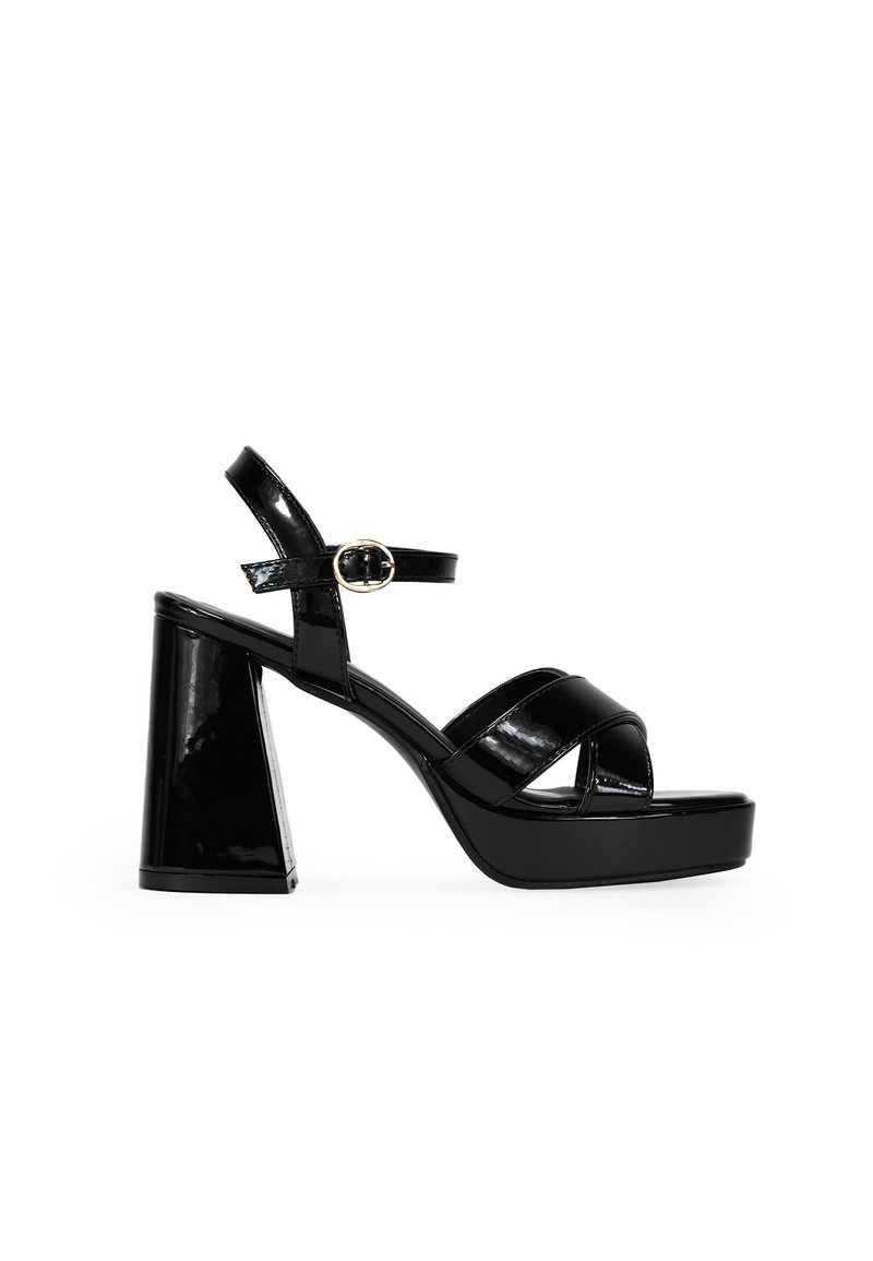 Sandalias de tacón alto de charol negro con un tacón grueso, suela de plataforma y correa en el tobillo con un detalle de hebilla circular.