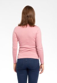 Maglietta a maniche lunghe, aderente, in morbido cotone rosa, con scollo rotondo. Abbinata a jeans blu scuro, con dettagli sulla cucitura posteriore visibili.