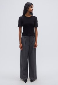 Μαύρο πλεκτό τοπ με κοντά μανίκια σε συνδυασμό με γκρι ψηλόμεση παντελόνα με φαρδιά μπατζάκια· εφαρμοστή γραμμή με λεπτές πιέτες, λείο ύφασμα και μυτερά τακούνια.