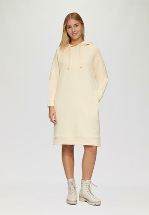 Hoodie jurk in licht perzikkleur met lange mouwen en geribbelde manchetten. Gecombineerd met roomkleurige veterschoenen en een losse pasvorm.